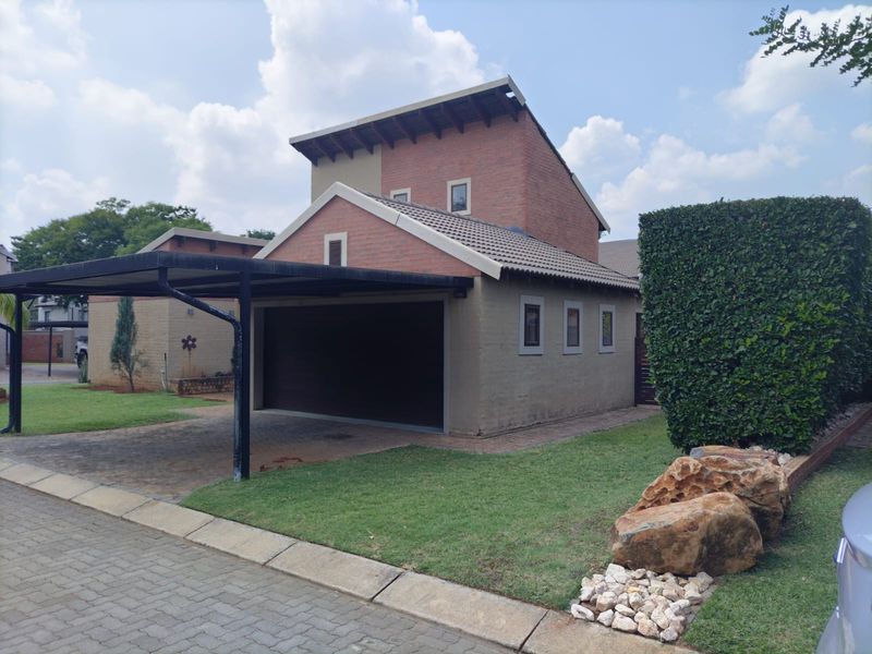 Front view of a residential property featuring a double garage, attached carport, paved driveway, and well-maintained garden area.