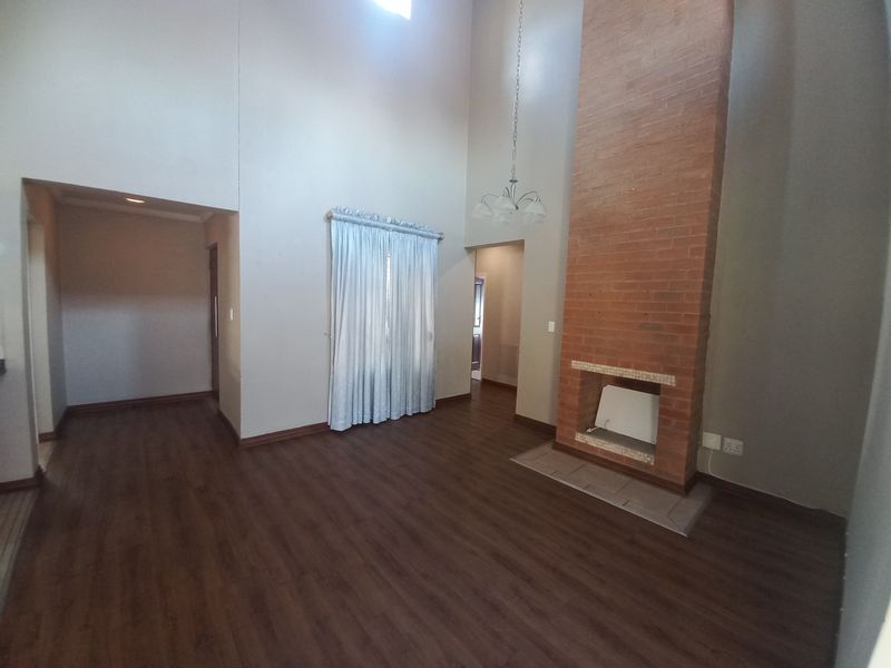 Spacious living room featuring a prominent brick fireplace, high vaulted ceilings, and dark laminate flooring in a neutral, open-plan layout.