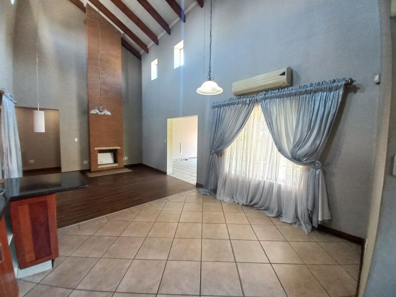 Spacious living area featuring vaulted ceilings with exposed timber beams, a built-in fireplace, and a mix of tiled and laminate flooring.