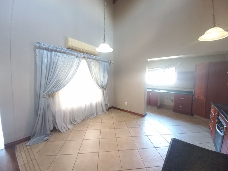 Spacious open-plan living and kitchen area featuring high vaulted ceilings, tiled flooring, and built-in cabinetry with integrated appliances.
