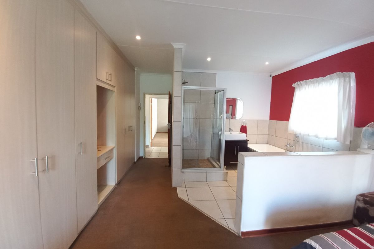 Spacious bedroom featuring an open-plan en-suite bathroom with a shower, vanity basin, and extensive built-in cupboard storage.