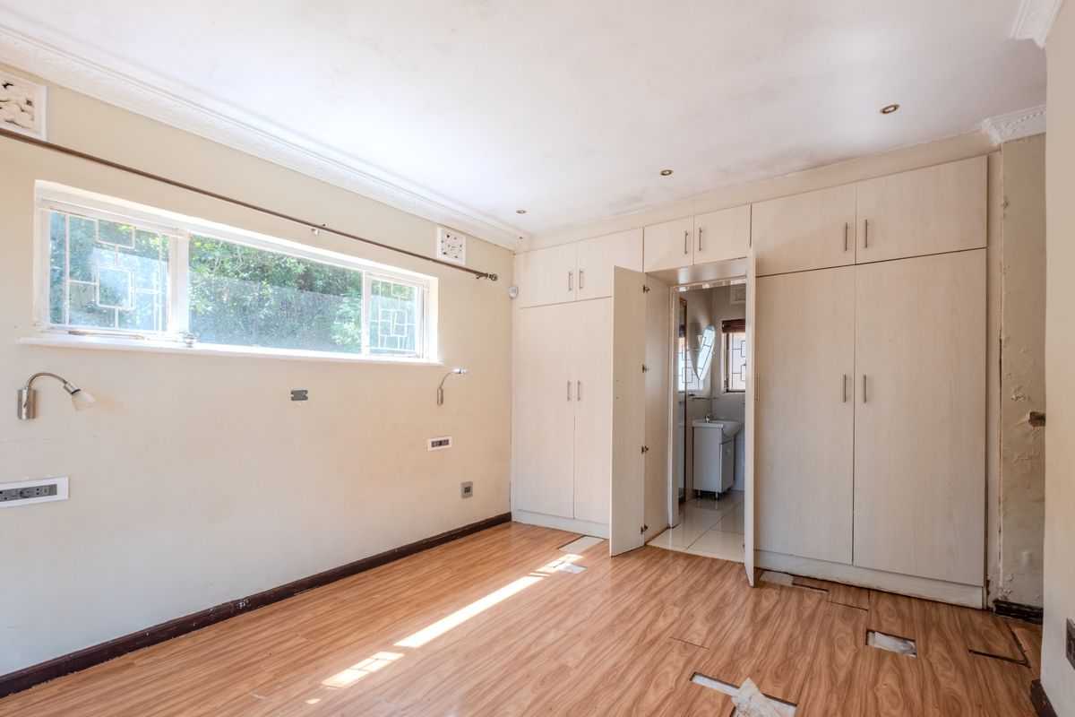 An empty bedroom featuring built-in cupboards, laminate flooring, and recessed lighting, requiring cosmetic repairs to the ceiling and flooring.