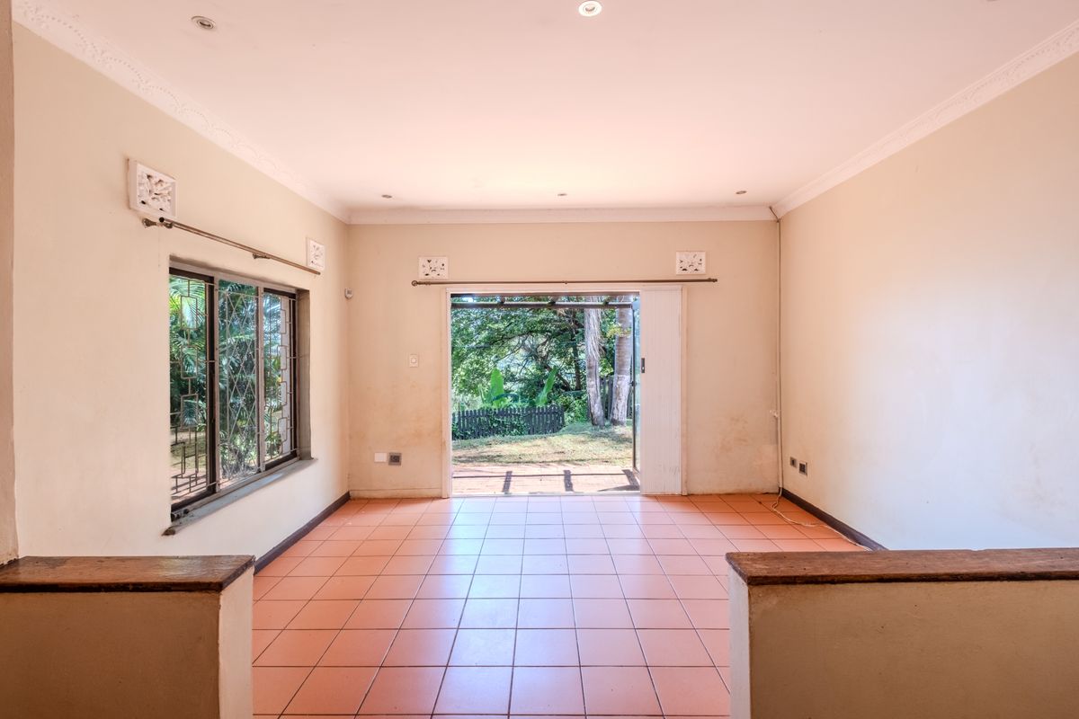 An empty living room featuring tiled flooring, recessed lighting, and a sliding glass door providing direct access to the garden area.