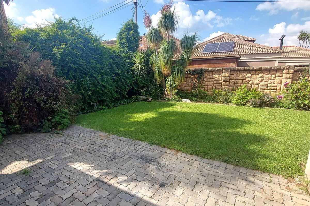 A private rear garden featuring a paved patio area, well-maintained lawn, and stone boundary wall.