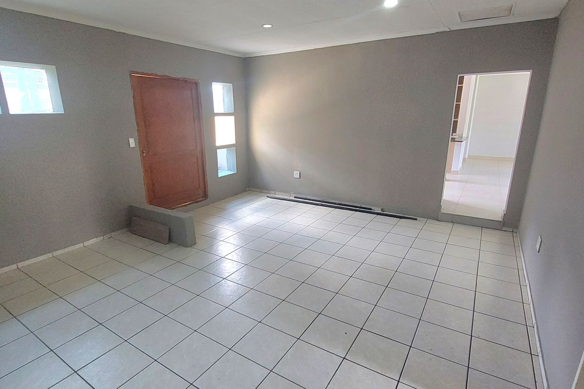 An empty living room featuring neutral grey walls, tiled flooring, and recessed ceiling lighting, offering a blank canvas for interior design.