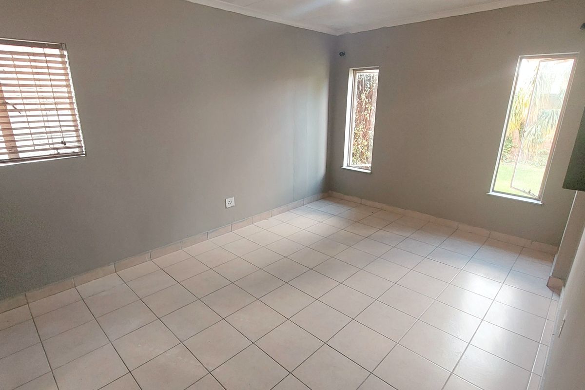 A bright, empty bedroom featuring neutral grey walls, tiled flooring, and multiple windows providing natural light.