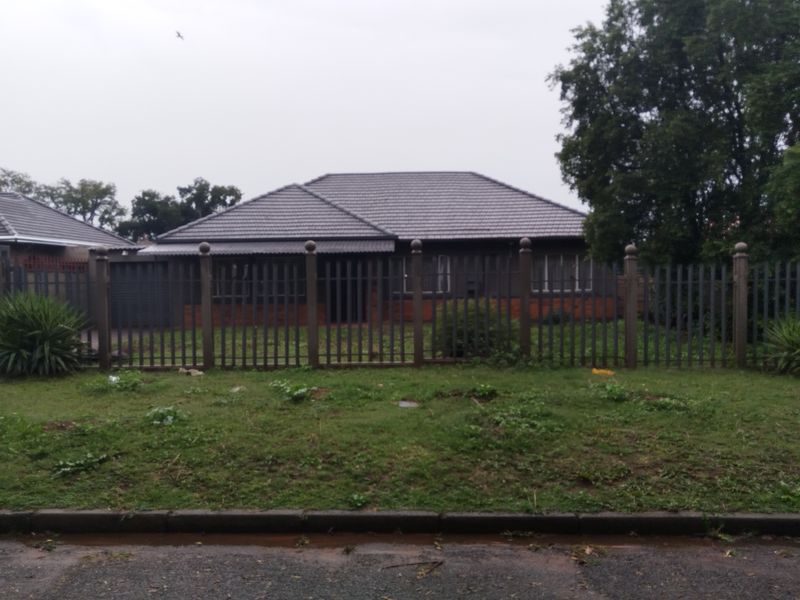 Front view of a single-story residential house featuring a tiled roof, brick exterior, and secure metal perimeter fencing with a front garden area.