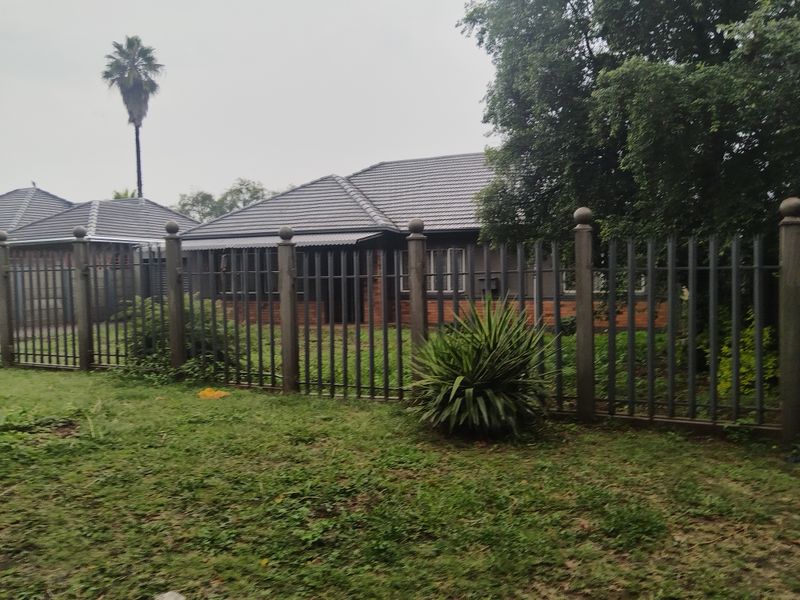 Front view of a single-story brick house featuring a tiled roof and secure metal perimeter fencing with a front garden.