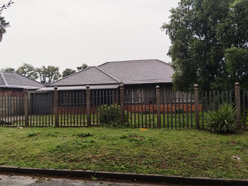 Front view of a single-story house featuring a tiled roof, brick accents, and secure metal perimeter fencing with a driveway.