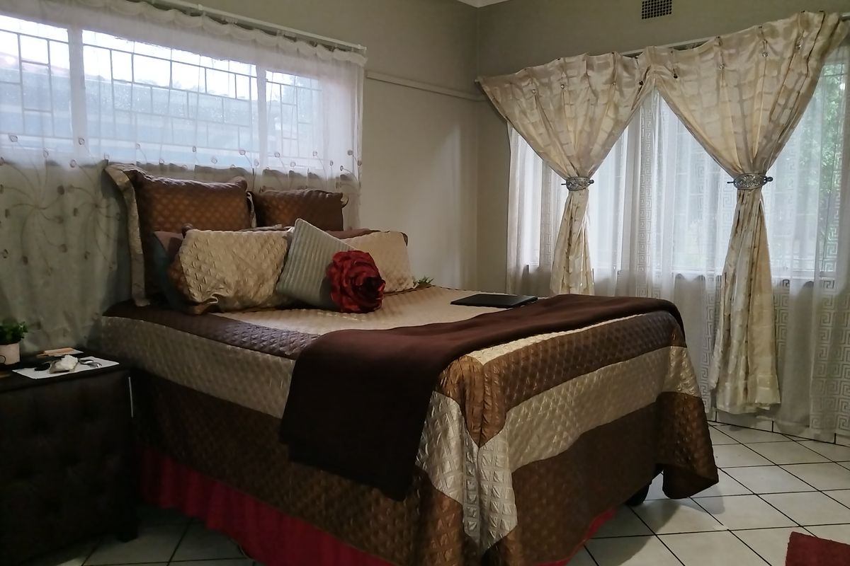 A well-lit bedroom featuring tiled flooring, large windows with security bars, and neutral wall finishes, providing a comfortable and functional sleeping space.