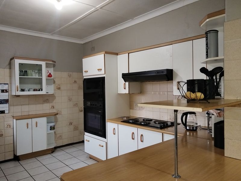 A functional kitchen featuring built-in cabinetry, an integrated oven, electric hob, extractor fan, and tiled splashbacks with a breakfast bar area.