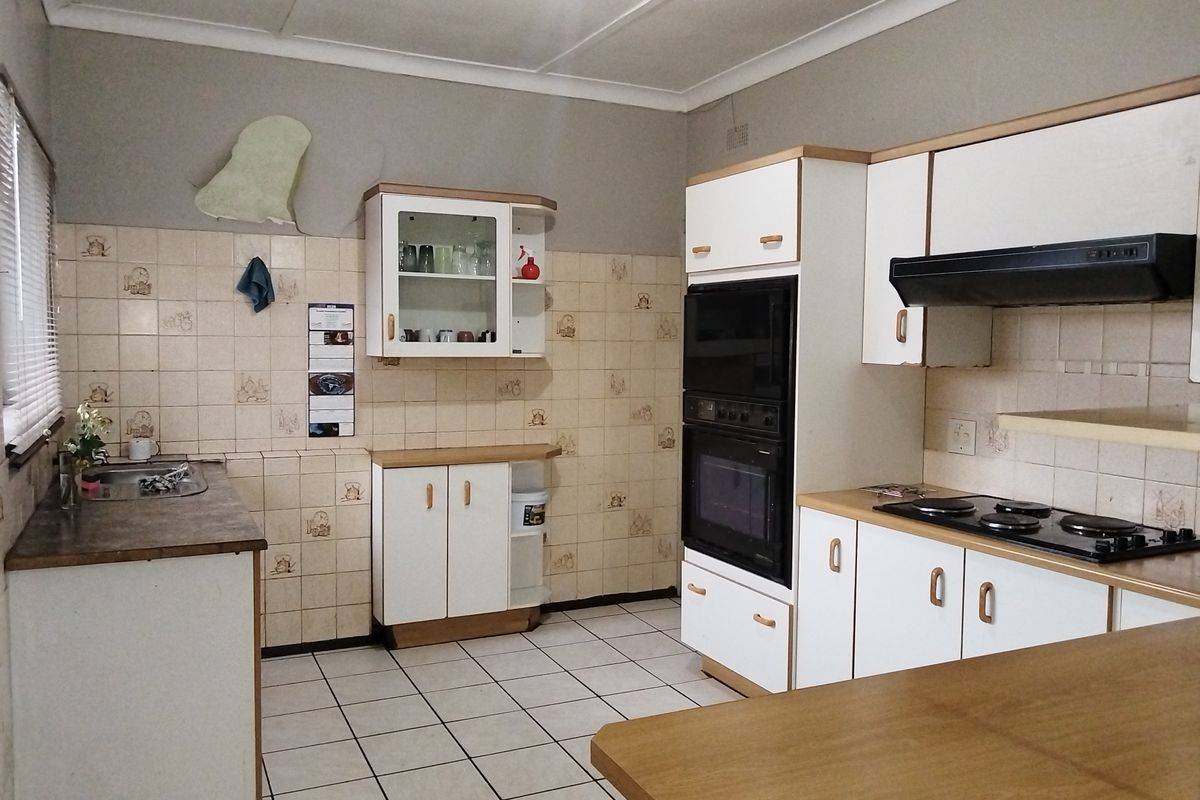A dated kitchen featuring built-in cabinetry, an integrated oven, electric hob, extractor fan, and tiled splashbacks, offering significant potential for modernization.