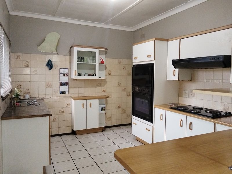 A dated kitchen featuring built-in cabinetry, an integrated oven, electric hob, extractor fan, and tiled splashbacks, offering significant potential for modernization.