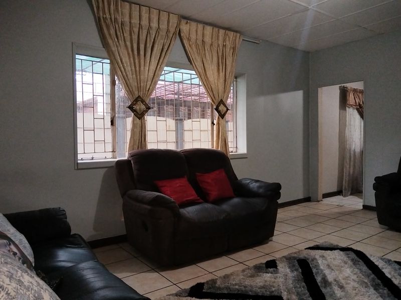 A living room featuring tiled flooring, security bars on the windows, and a drop ceiling, providing a functional and lived-in space.