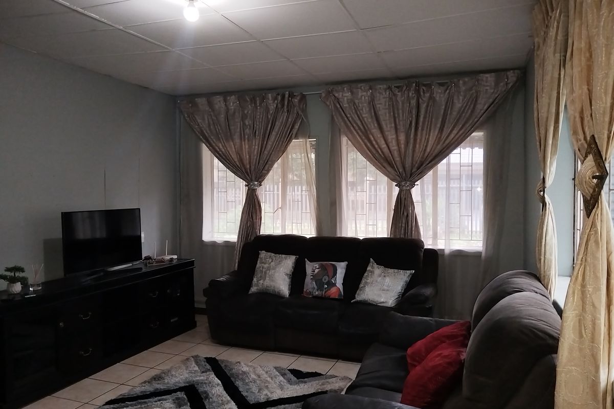 A living room featuring tiled flooring, security bars on windows, and a drop ceiling, offering a functional space with potential for cosmetic updates.