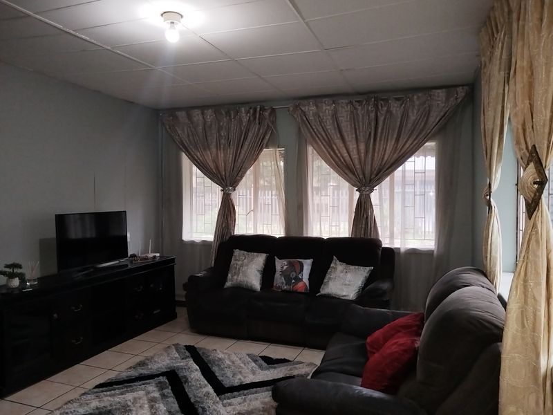 A living room featuring tiled flooring, security bars on windows, and a drop ceiling, offering a functional space with potential for cosmetic updates.
