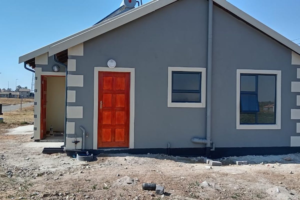 A view of the rear exterior of a modern house featuring grey painted walls with contrasting quoins, timber door, and aluminium window frames.