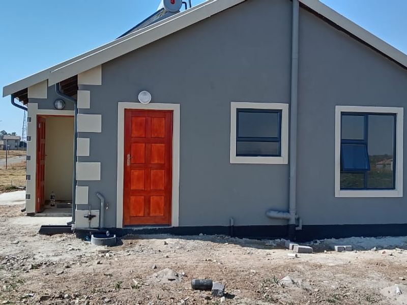 A view of the rear exterior of a modern house featuring grey painted walls with contrasting quoins, timber door, and aluminium window frames.