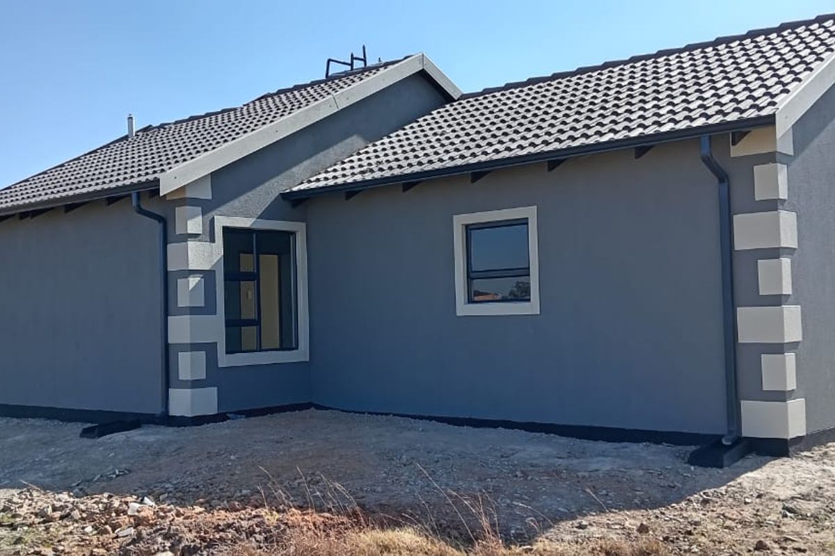 Rear view of a modern single-story house featuring grey textured plaster walls, contrasting corner quoins, and a tiled roof with installed guttering.