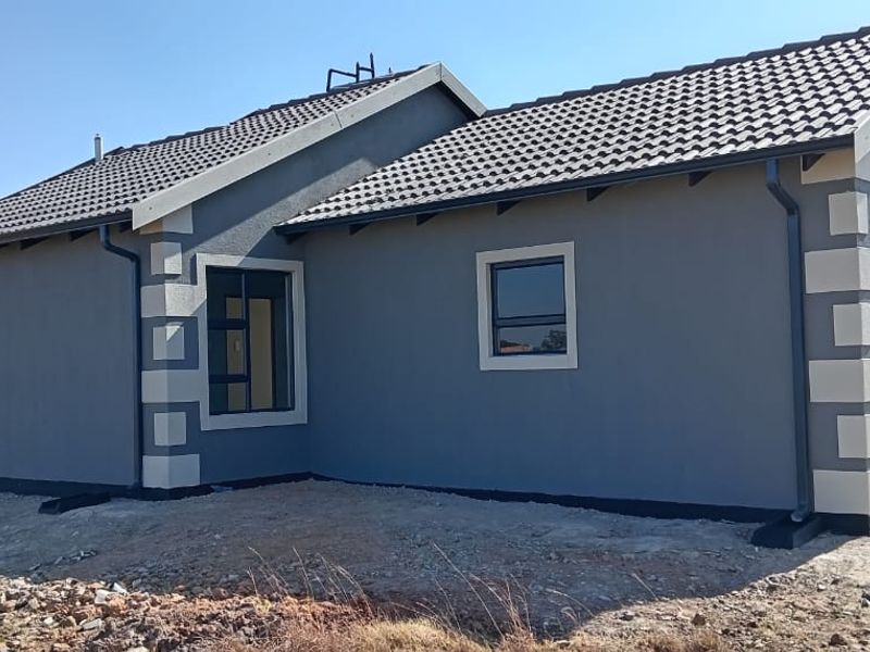 Rear view of a modern single-story house featuring grey textured plaster walls, contrasting corner quoins, and a tiled roof with installed guttering.