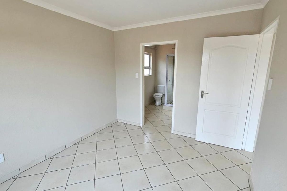 A clean, empty bedroom featuring neutral tiled flooring, coved ceilings, and direct access to an en-suite bathroom.