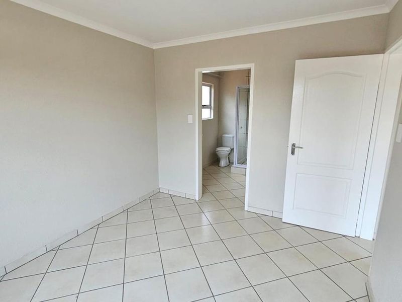 A clean, empty bedroom featuring neutral tiled flooring, coved ceilings, and direct access to an en-suite bathroom.
