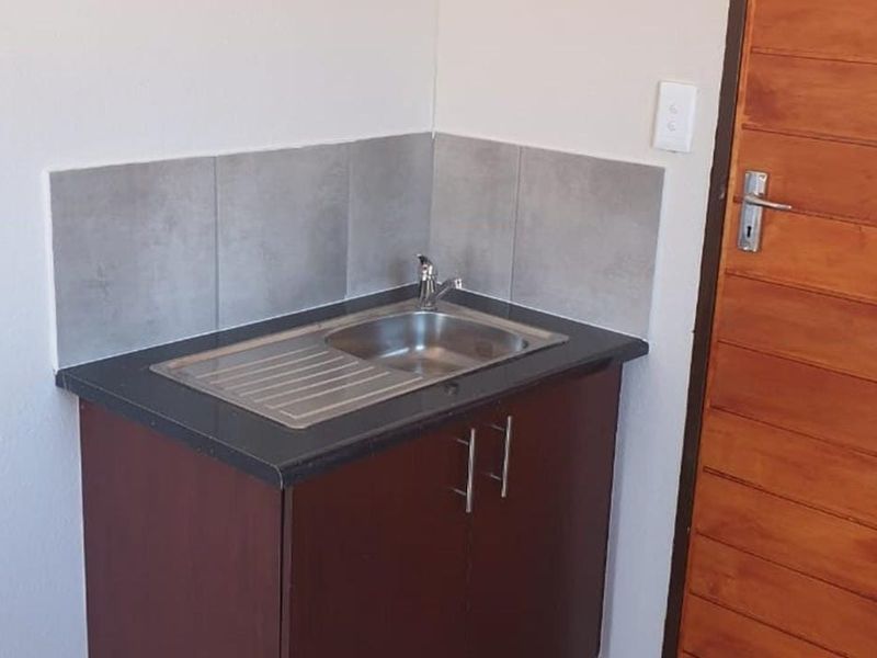A compact scullery or utility area featuring a stainless steel sink, dark laminate countertop, base cabinetry, and a tiled splashback.