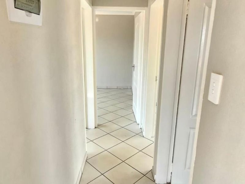 A clean, neutral hallway featuring tiled flooring and multiple internal doors providing access to adjacent rooms.