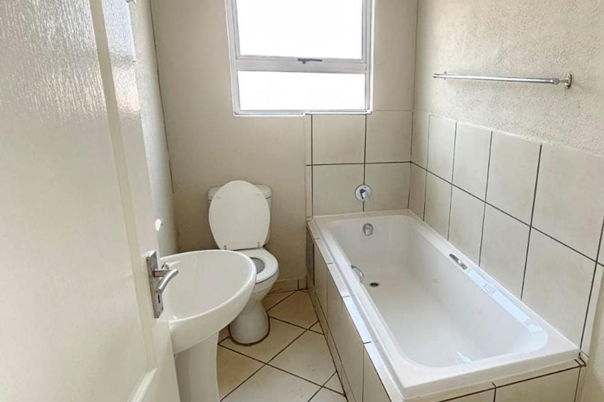 A functional bathroom featuring a pedestal basin, toilet, and a built-in bathtub with tiled splashbacks, offering a clean and simple layout.