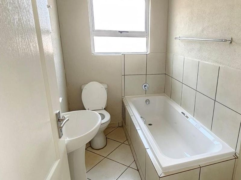 A functional bathroom featuring a pedestal basin, toilet, and a built-in bathtub with tiled splashbacks, offering a clean and simple layout.