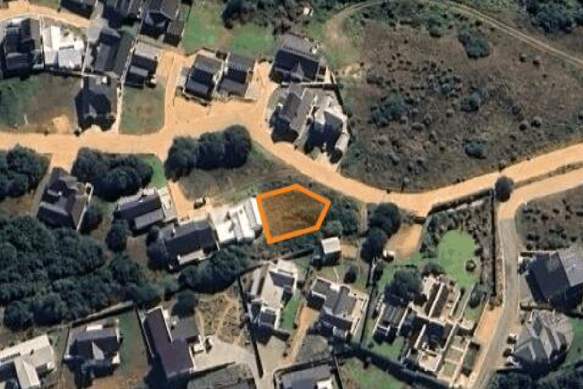 An aerial view of a vacant residential land plot situated within a developed coastal estate.
