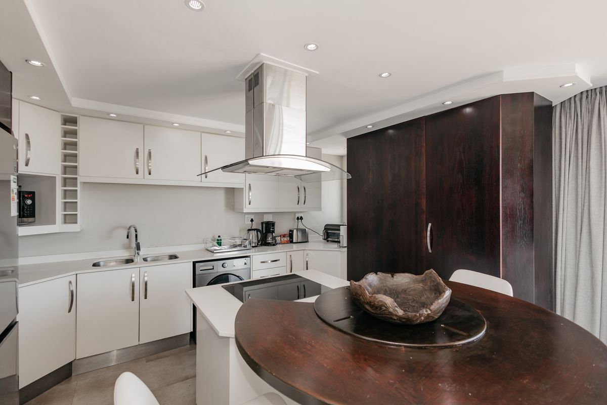 Modern kitchen featuring white cabinetry, stone countertops, integrated hob, stainless steel extractor fan, and a contrasting dark wood pantry unit.