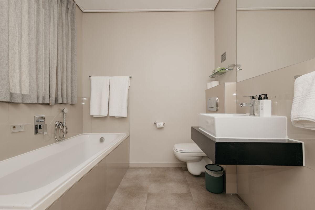 Modern bathroom featuring a built-in bathtub, wall-mounted toilet, and a floating vanity with a vessel sink, finished with neutral wall tiles.