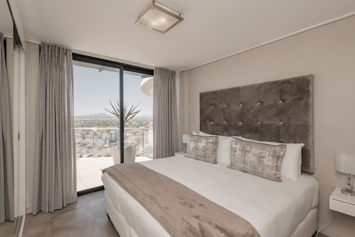 Modern bedroom featuring tiled flooring, a built-in ceiling light, and large sliding glass doors providing access to a balcony with expansive city views.