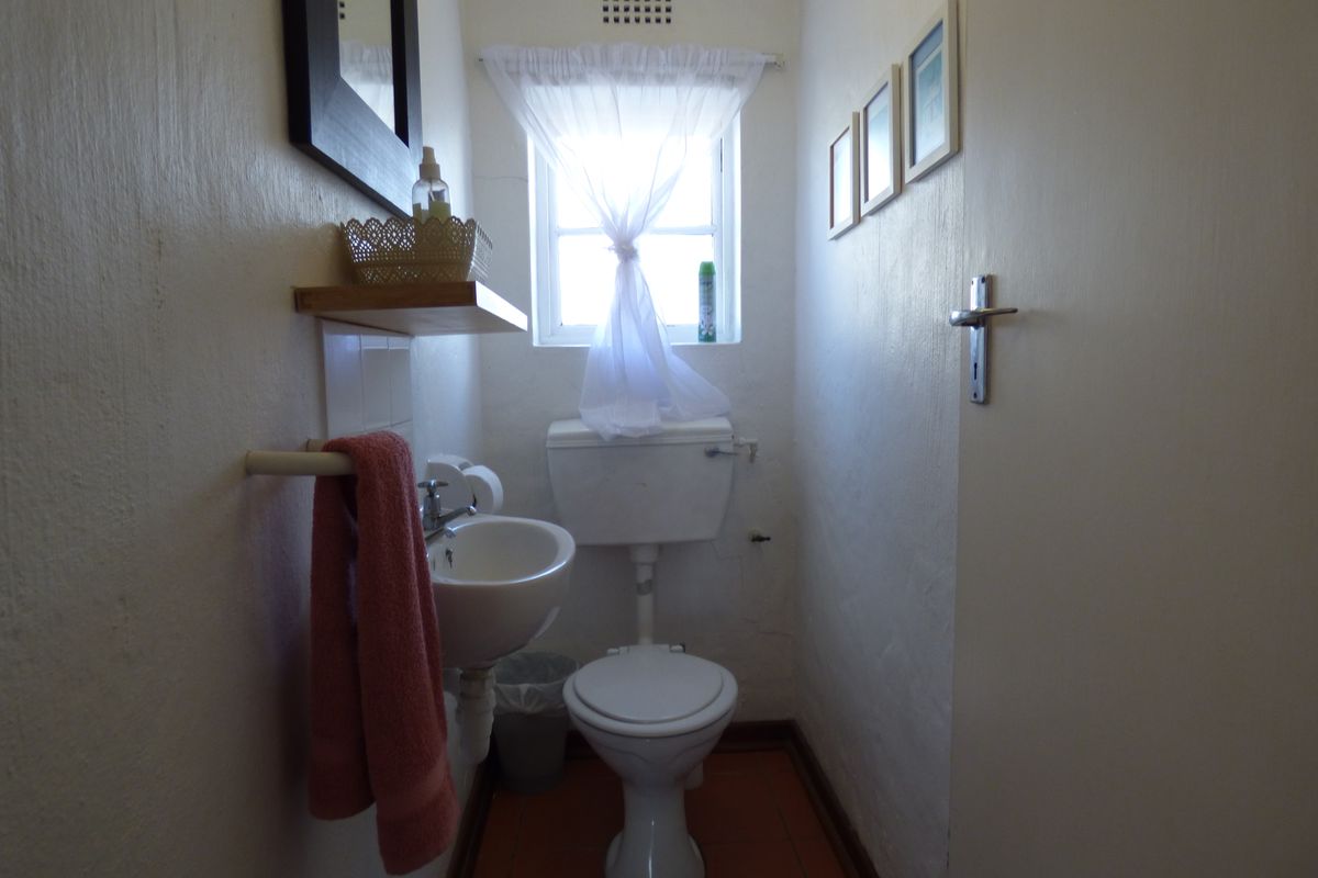 A compact guest bathroom featuring a wall-mounted basin, toilet, and tiled flooring, requiring cosmetic updates to improve its overall condition.