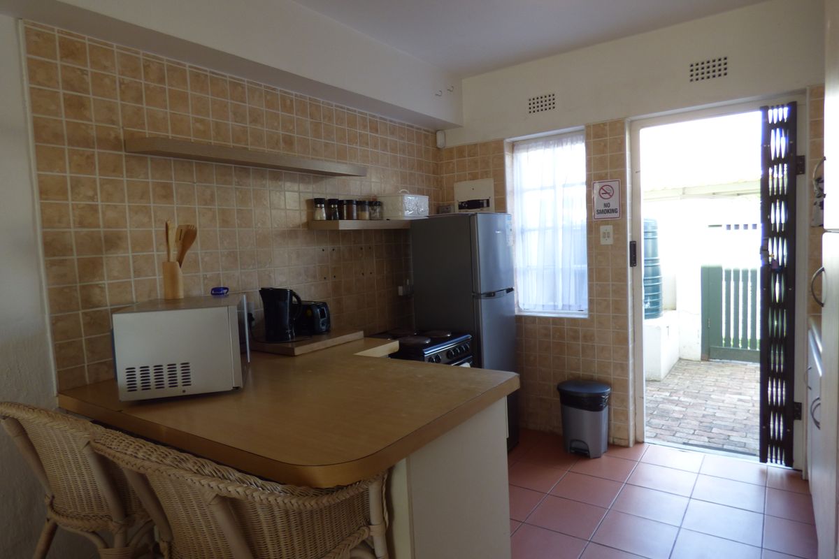 A functional kitchen featuring tiled splashbacks, laminate countertops, and an electric stove, with direct access to an outdoor paved area.
