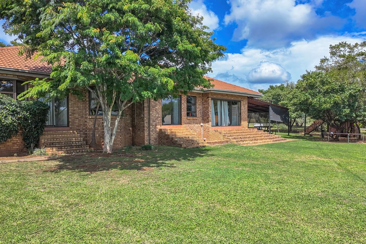 Rear view of a face brick house featuring a tiled roof, sliding glass doors, and a spacious garden with a covered patio area.