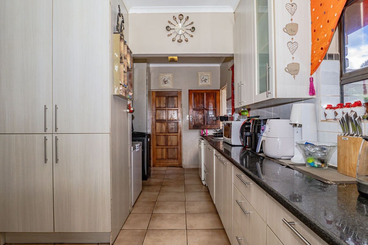 A functional kitchen featuring granite countertops, ample built-in cabinetry, and tiled flooring, leading through to a traditional timber panel door.
