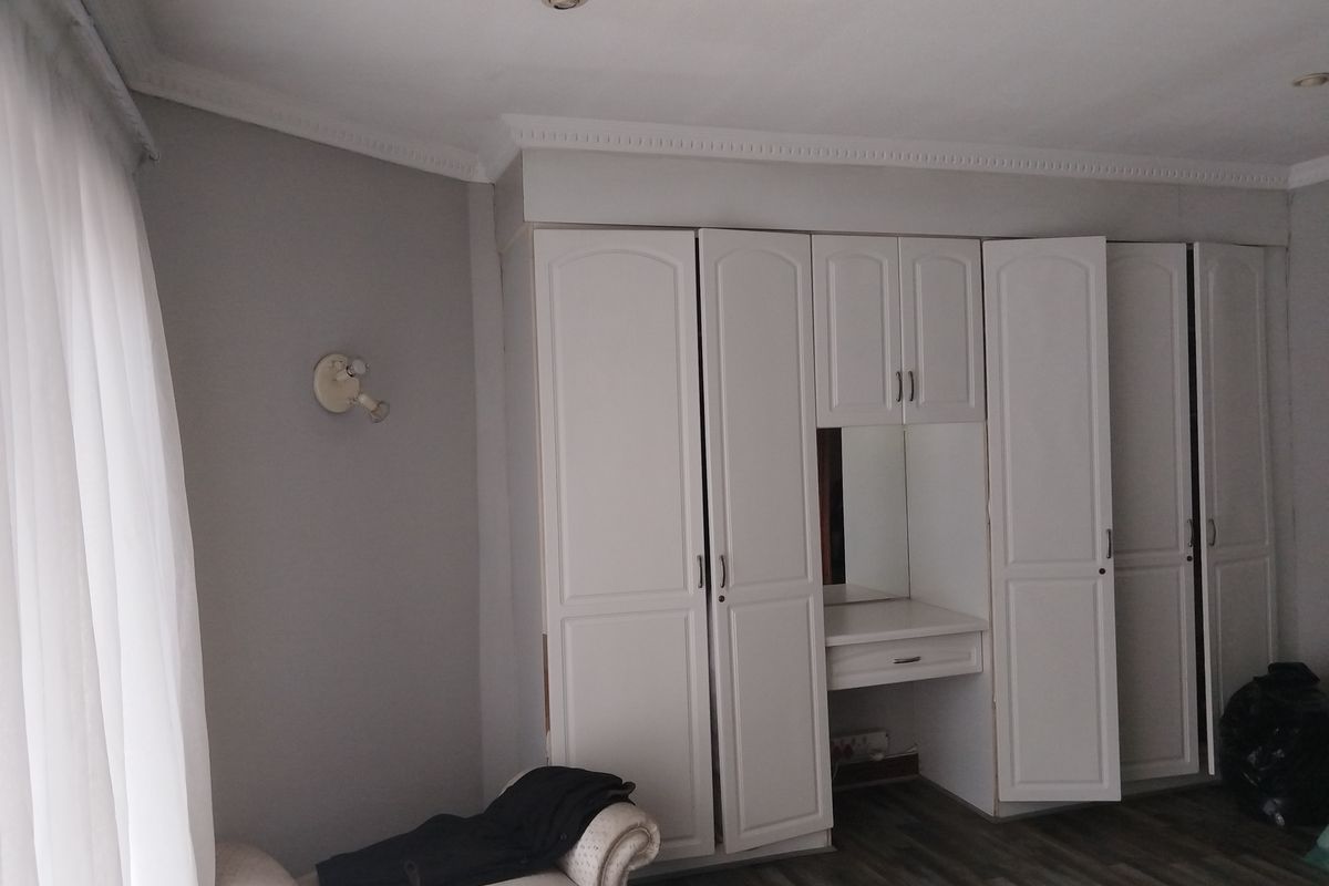 Bedroom featuring extensive white built-in cupboards with an integrated vanity unit, recessed ceiling lighting, and modern laminate flooring.