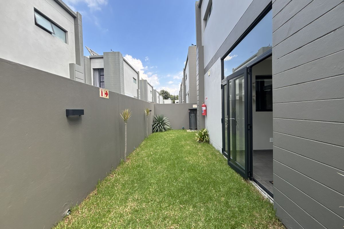 A private rear garden area featuring a well-maintained lawn, boundary walls, and direct access to the interior through modern glass sliding doors.