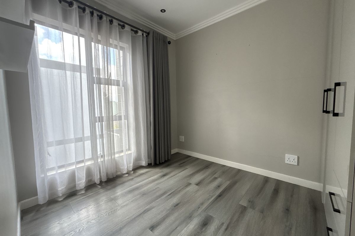 A bright, empty bedroom featuring modern laminate flooring, built-in cupboards, and neutral grey walls, offering a clean and versatile space.