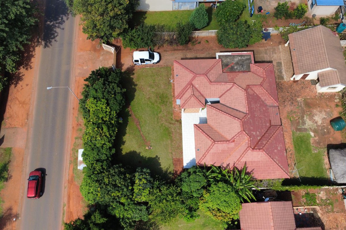 Aerial view of the property showing the main house with a tiled roof, surrounding garden, and paved driveway access from the street.