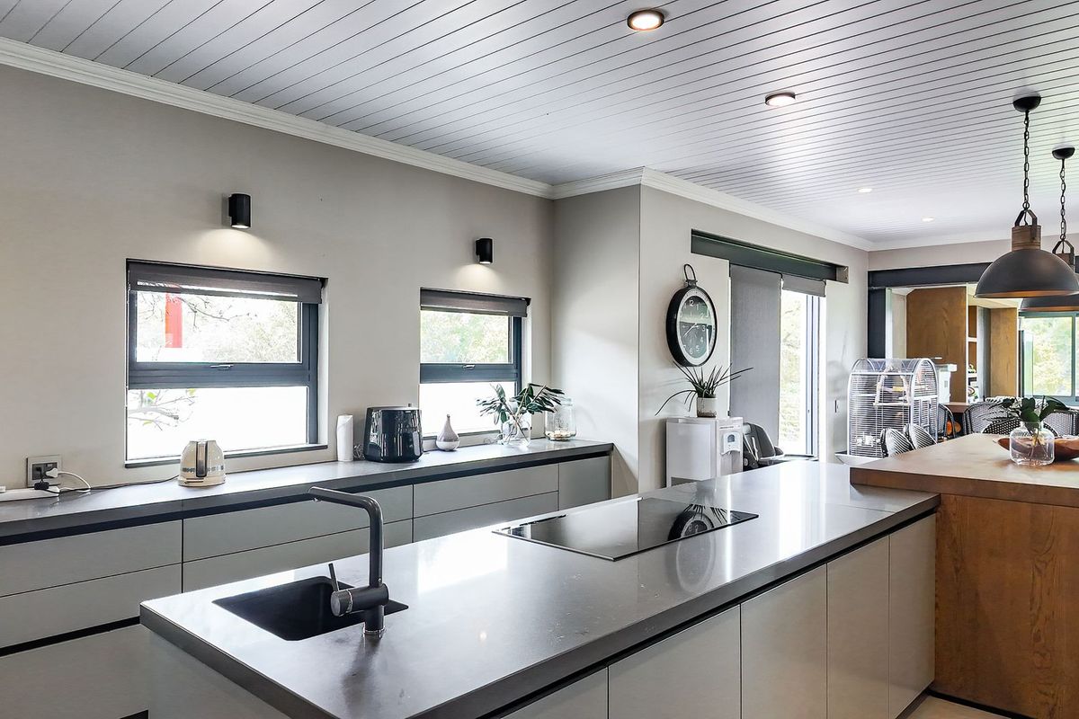 Modern kitchen featuring a large central island with integrated cooktop, sleek cabinetry, stone countertops, and contemporary pendant lighting.