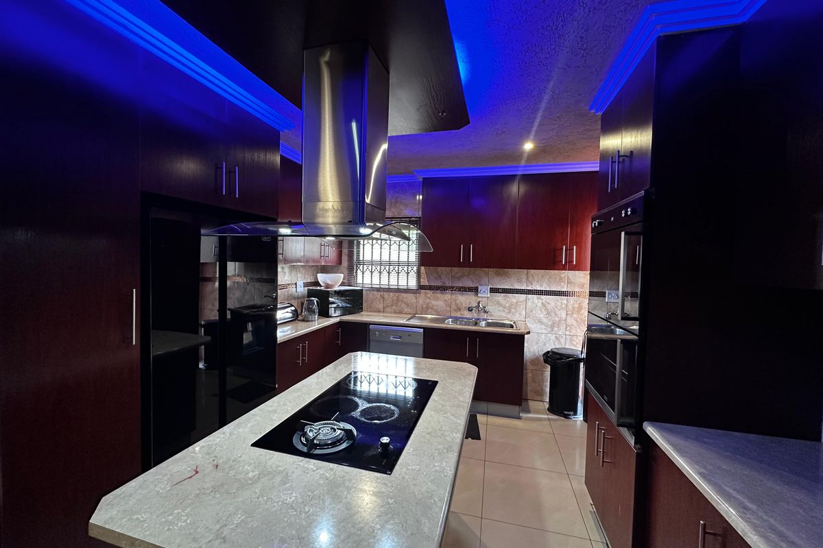 Modern kitchen featuring dark wood cabinetry, a central island with a built-in hob, stainless steel extractor fan, and integrated oven.