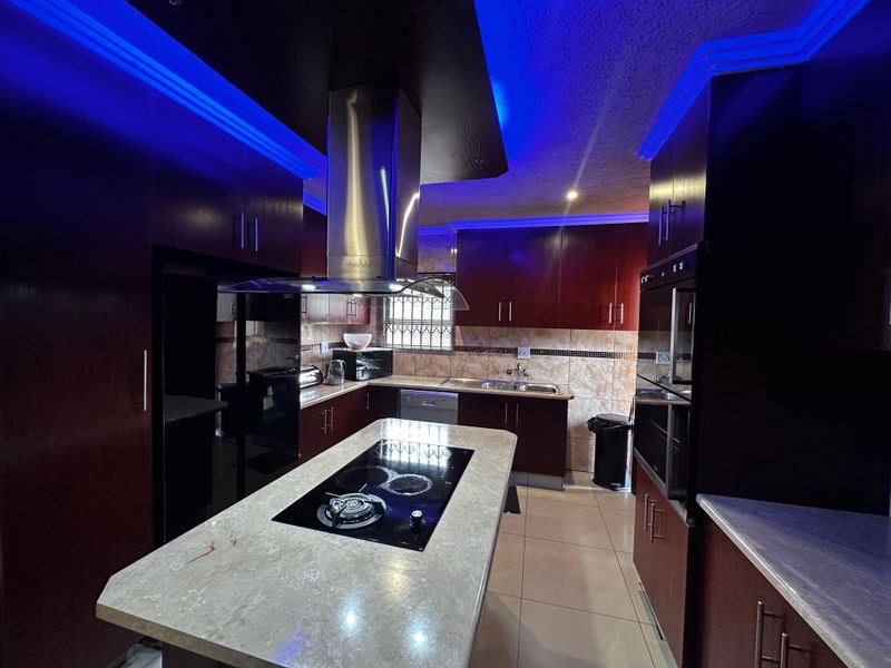 Modern kitchen featuring dark wood cabinetry, a central island with a built-in hob, stainless steel extractor fan, and integrated oven.