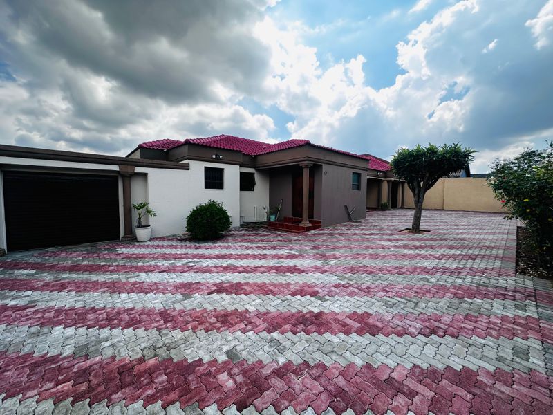 Front view of a residential property featuring a large patterned paved driveway, a single garage, and a covered entrance with a tiled roof.