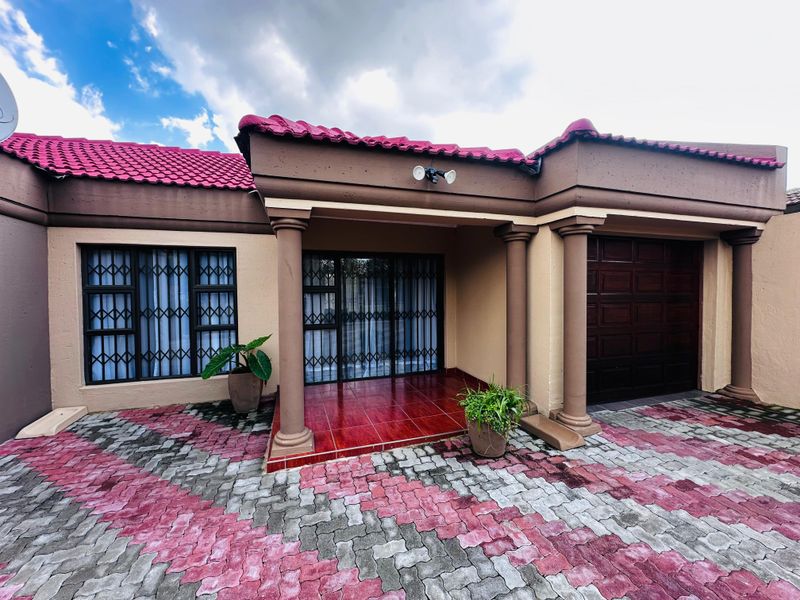 Front elevation of a house featuring a paved driveway, covered entrance porch with decorative columns, security gates, and an integrated single garage.