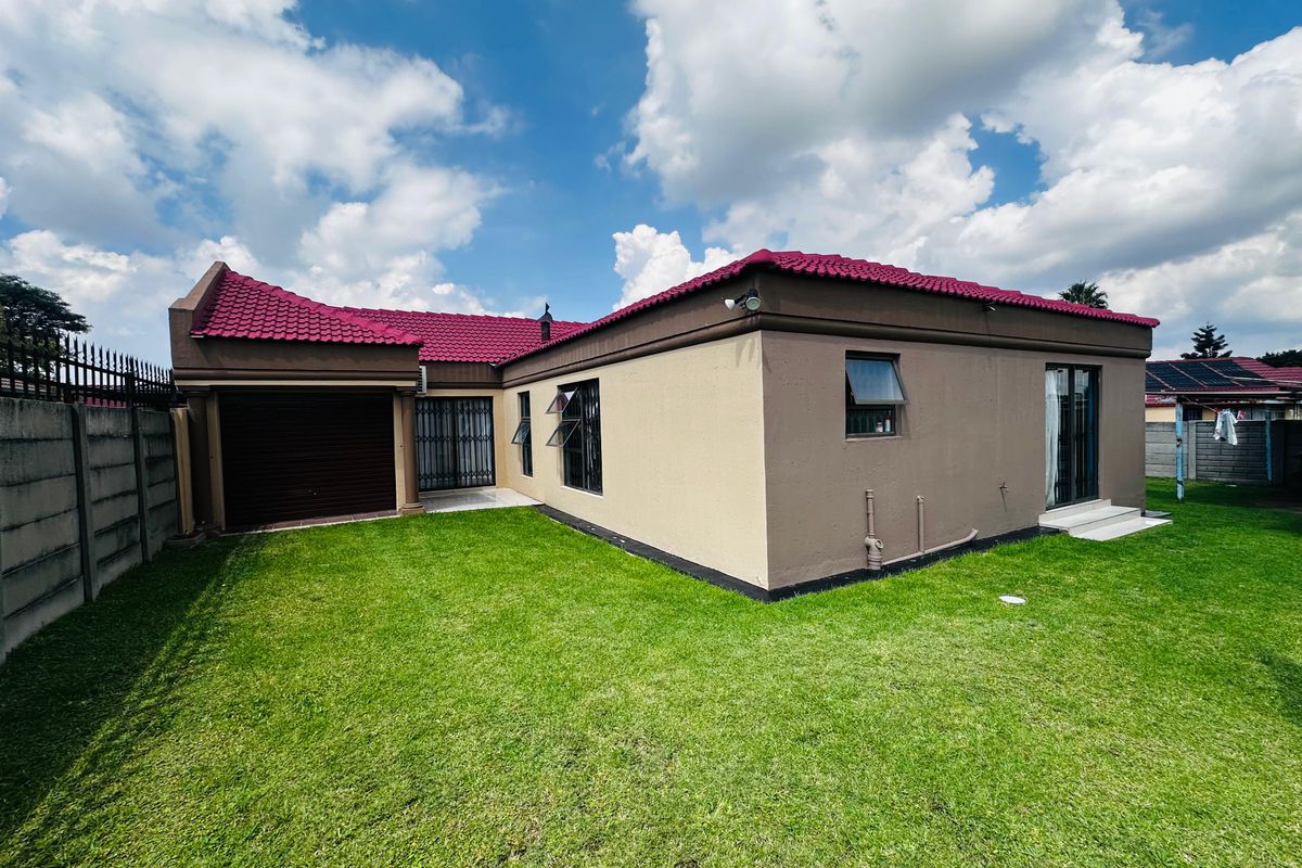 Rear view of the property featuring a well-maintained lawn, tiled roof, and secure boundary walling.