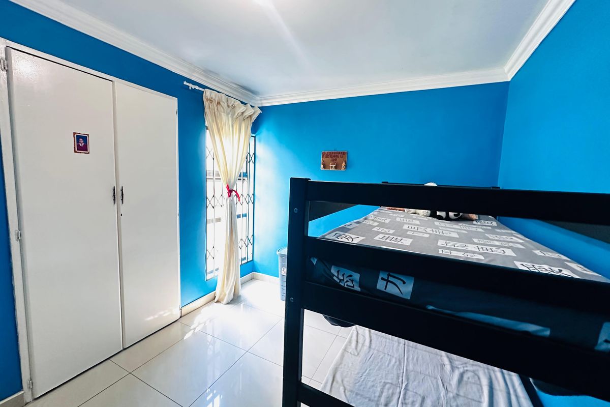 A bedroom featuring tiled flooring, built-in cupboards, and a security gate on the window.