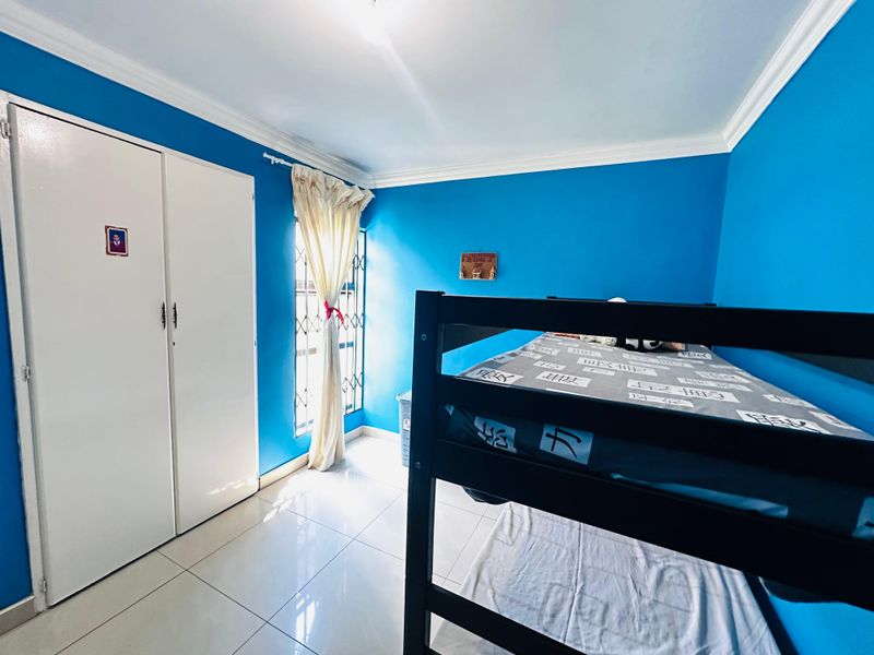 A bedroom featuring tiled flooring, built-in cupboards, and a security gate on the window.